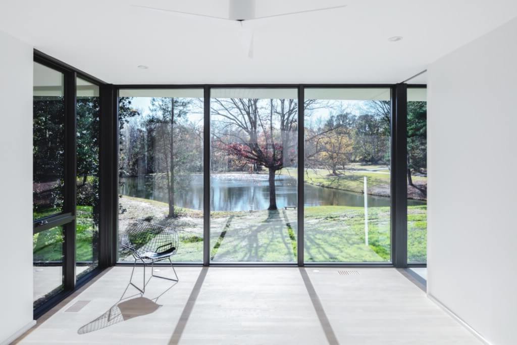 Modern sunroom with floor to ceiling windows viewing a backyard with a pond