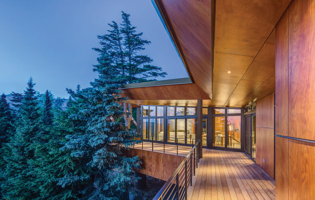 Long outdoor hallway leading to room surrounded by windows and trees